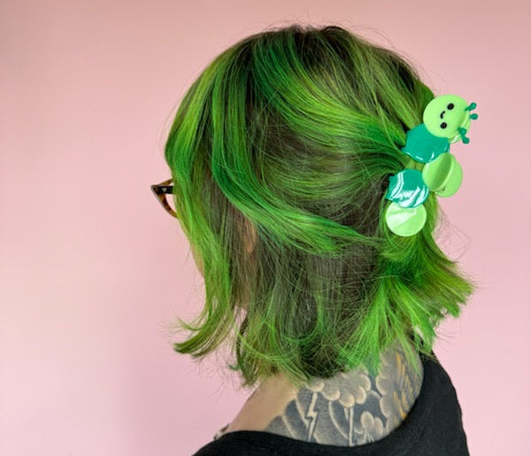 Person with green hair wearing a hair clip against a pink background